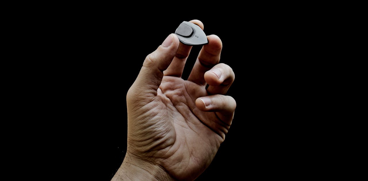 A detailed close-up photo of a hand holding a guitar pick against a black background.