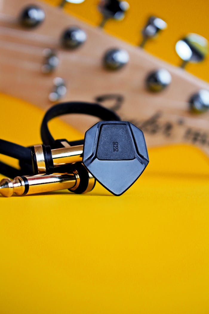 Guitar cable and pick on vibrant yellow backdrop, perfect for music themes.